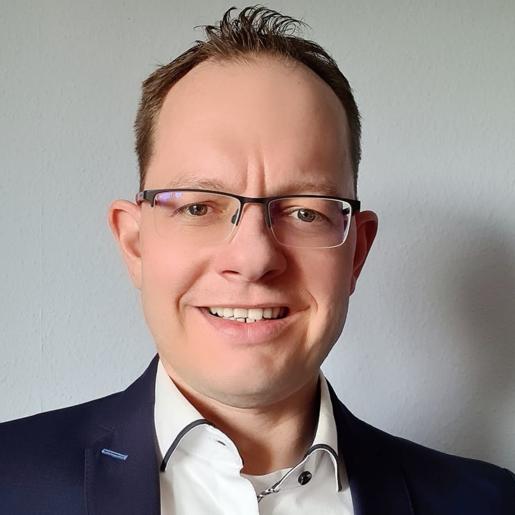 Evigo® Eine Person Mit Brille Und Dunklem Anzug Lächelt In Die Kamera Und Strahlt Das Selbstvertrauen Und Die Professionalität Aus, Die Man Von Jemandem Erwartet, Der Gerade Ein Innovatives Kundenportal Gestartet Hat.